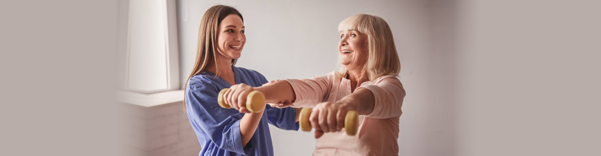 smiling female caregiver and her old woman patient doing exercise