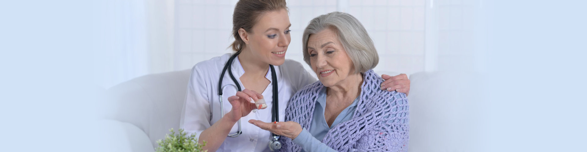 female caregiver with stethoscope giving medicine to her old woman patient